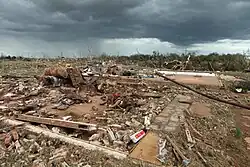 Concrete slab foundations of homes are covered in shredded debris, with a dark and cloudy sky behind them.