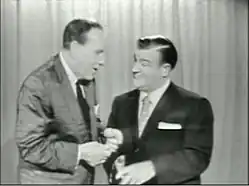 two men stand in front of a curtain speaking to each other