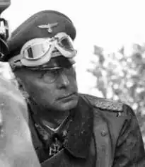 The head and torso of a man wearing a military uniform and overcoat; an Iron Cross is displayed at the front of his uniform collar.