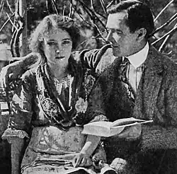A man reading to a blind woman seated next to him