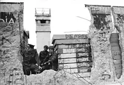 East German border guards look through a hole in the Berlin Wall in 1990