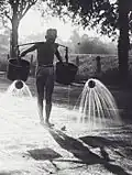 A worker waters a road in the Dutch East Indies
