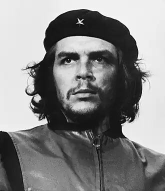 Black and white image of a long-haired, bearded man of about 30, wearing a military beret and vest