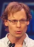 A man speaking into a microphone looking at the viewer