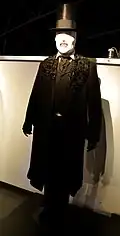 A white-skinned, eyeless, sharp-toothed humanoid figure wearing darkly colored Victorian garb and a top hat.