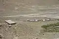 A view of Everest North Base Camp looking west, August 3, 2002. The permanent structure at left is for mountain climbers, central-left structure is for pit toilets, while the temporary wood-frame, plastic tarpaulin-covered structures below and right are for other visitors and support people.