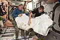 Anchored by their toes, Expedition 47 Commander Tim Kopra and Flight Engineer Tim Peake wrestle an M/D Cover Center Section into the vestibule while preparing for deberth of a Cygnus cargo vehicle from Node 1 (Unity).