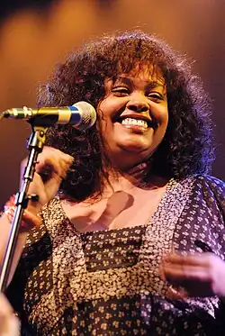 A woman wearing a brown dress while smiling and snapping her fingers.