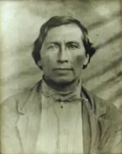 John Solomon with short, dark hair wearing a single-breasted jacket and a neckerchief.