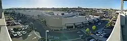 Panorama of west side of La Jolla Village Square, featuring a row of businesses and a large parking lot.