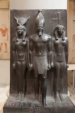Goddess representation in Egyptian monuments: in this triad the Egyptian goddess Hathor (left) and the nome goddess Bat (right) lead Pharaoh Menkaura (middle). Egypt, Fourth dynasty, about 2400&nbsp;BCE. Graywacke. Cairo Museum.