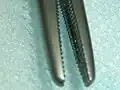 Close-up of a needle driver showing the cross-serrated teeth of its jaws