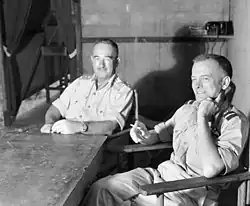 Two men in light-coloured uniforms seated at a table