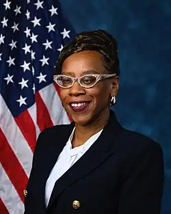 Official House portrait of Simon smiling in front of the U.S. flag, wearing a white shirt and black suit with large gold buttons.
