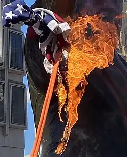A statue of Frank Rizzo that has been spray-painted and has a burning American flag attached to it with a rope