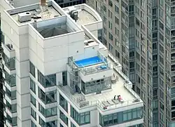A parapet surrounds a New York City rooftop, shielding the HVAC and water tank and supporting the glass guardrails.