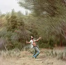 A man standing with his arms out inside a forest opening