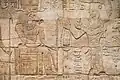 Taharqa and the gods of Gematen (the Temple of Kawa). He makes an offering to the ram-headed god Amun-Re. Kawa shrine.[64]