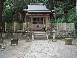 An image of Takijiri-oji shrine, the formal entryway into the holy land of Kumano. It is a wooden shrine building with stone lanterns in the front set against forested mountains.