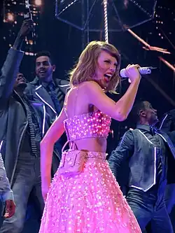 A young white woman singing on a microphone, wearing a polka-dot pink two piece dress