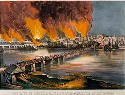 bridge in foreground going across river to city landscape that has flames reaching upwards